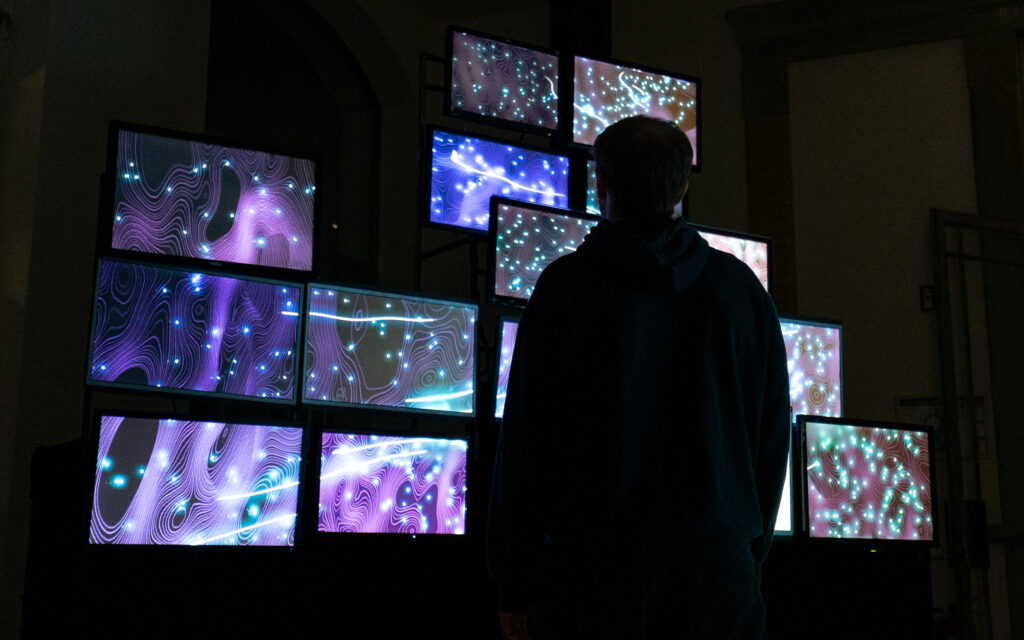 A person stands in front of a wall of screens.