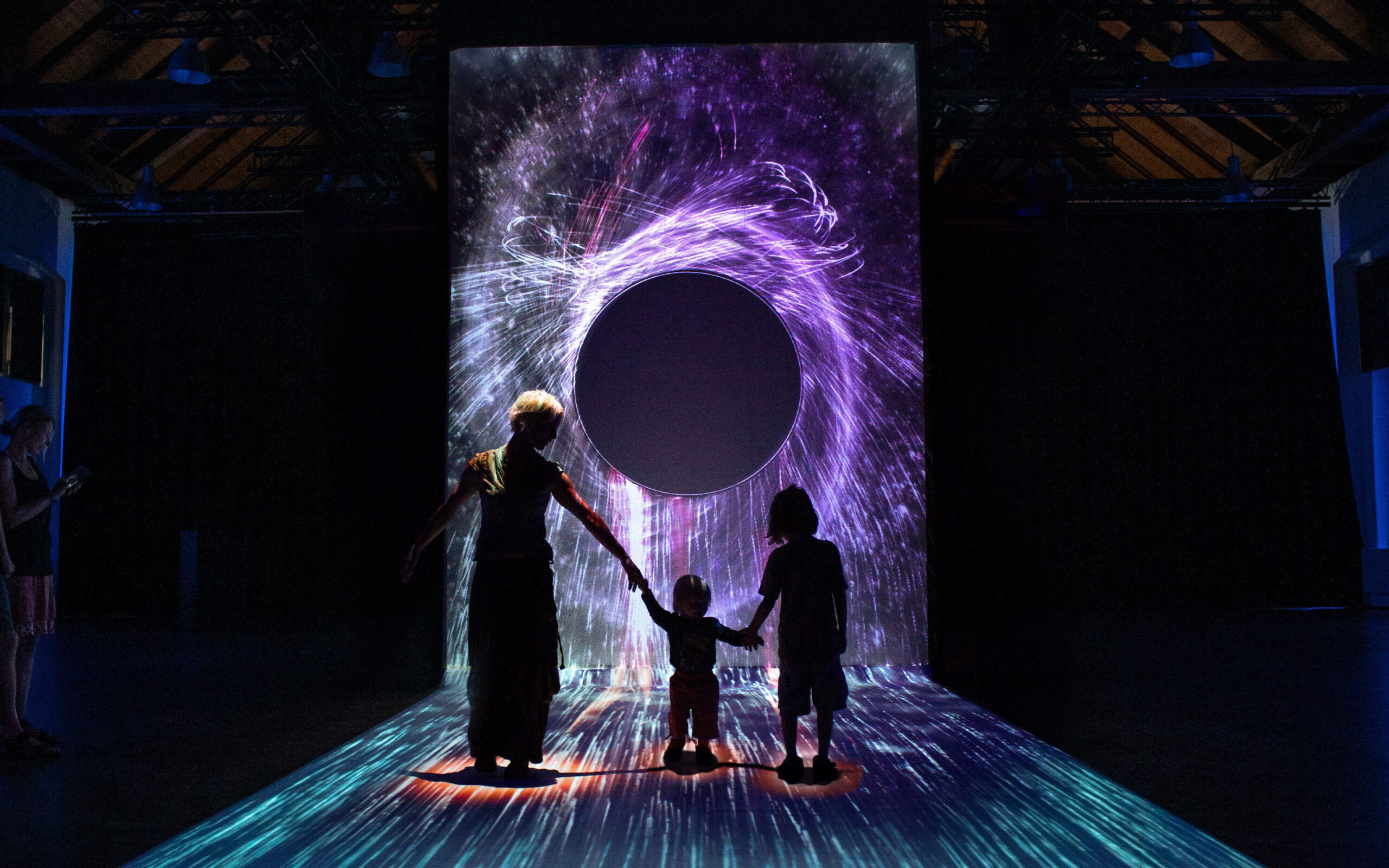 A family walks through an interactive projection of a black hole.