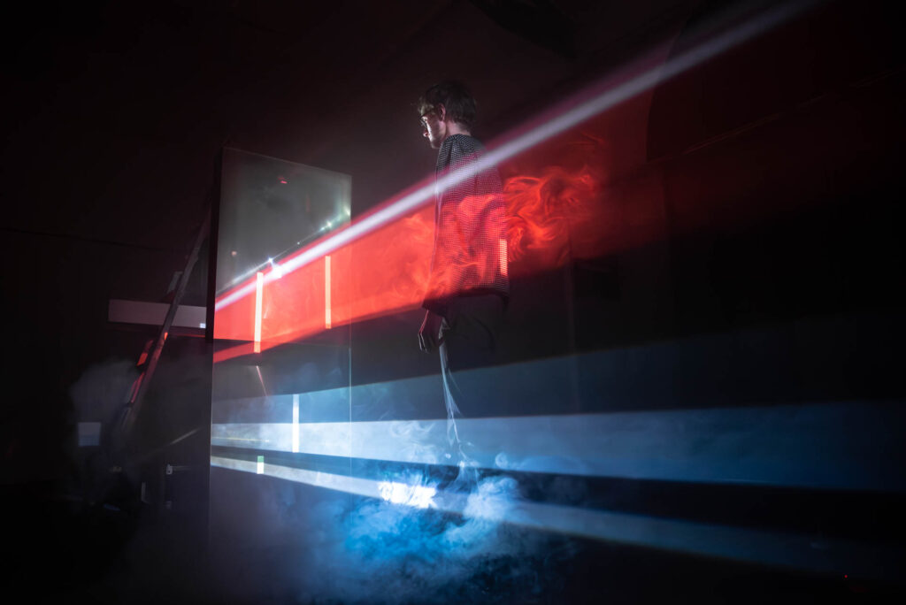 A person stands in front of light rays in red, blue and white.