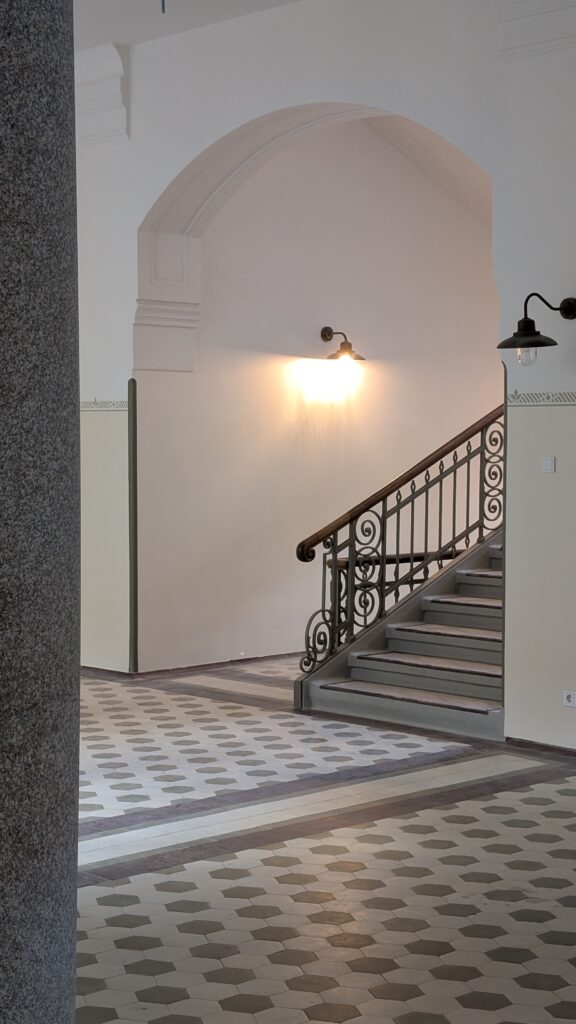 Eine restaurierte Treppe mit schmiedeeisernem Geländer über einem gemusterten Fliesenboden.