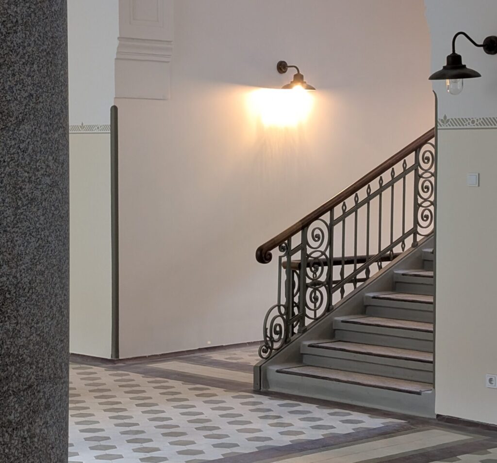 A restored staircase with a wrought-iron railing above a patterned tiled floor.