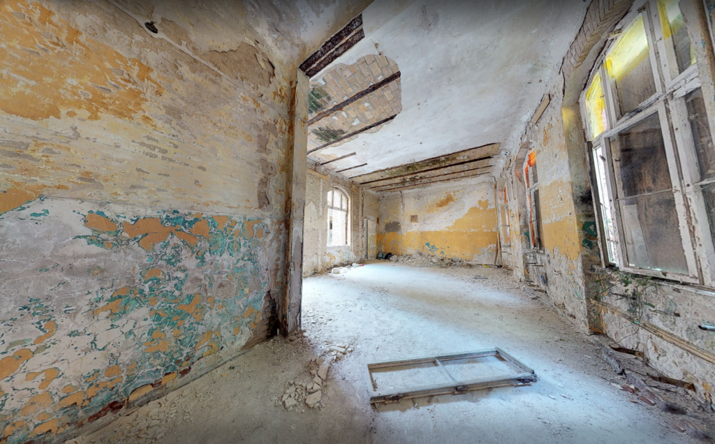 A decayed, dust-covered room in the building before restoration, with peeling paint on the walls.