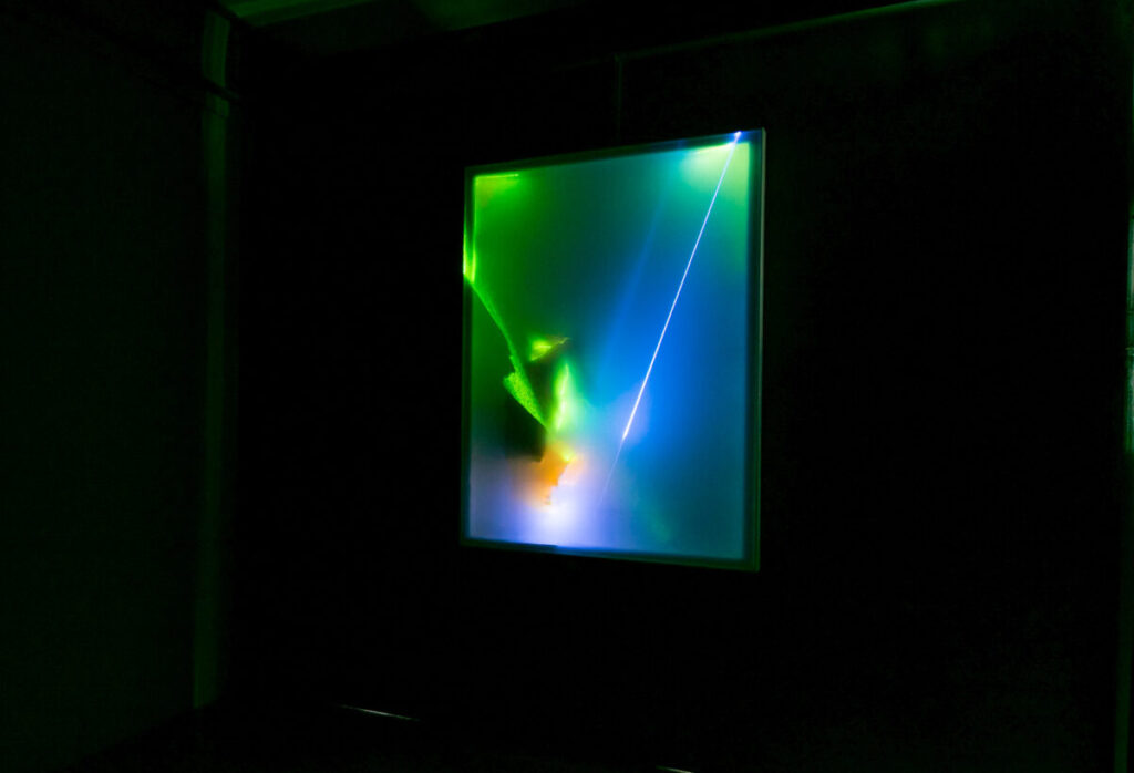 On a wall hangs an image made of blue, green and orange lasers.